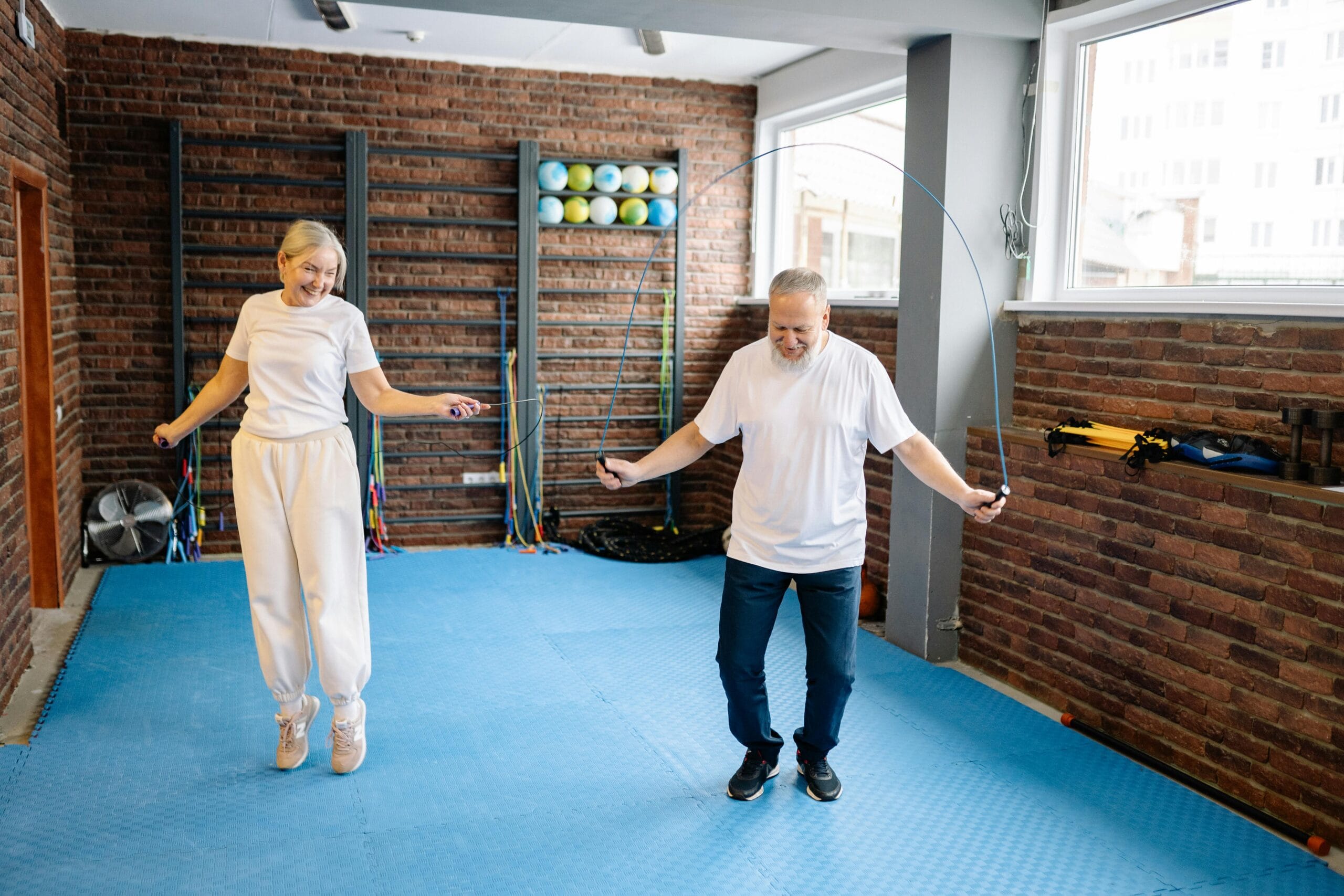A man and woman perform coordination exercises with a jump rope in a gym setting.