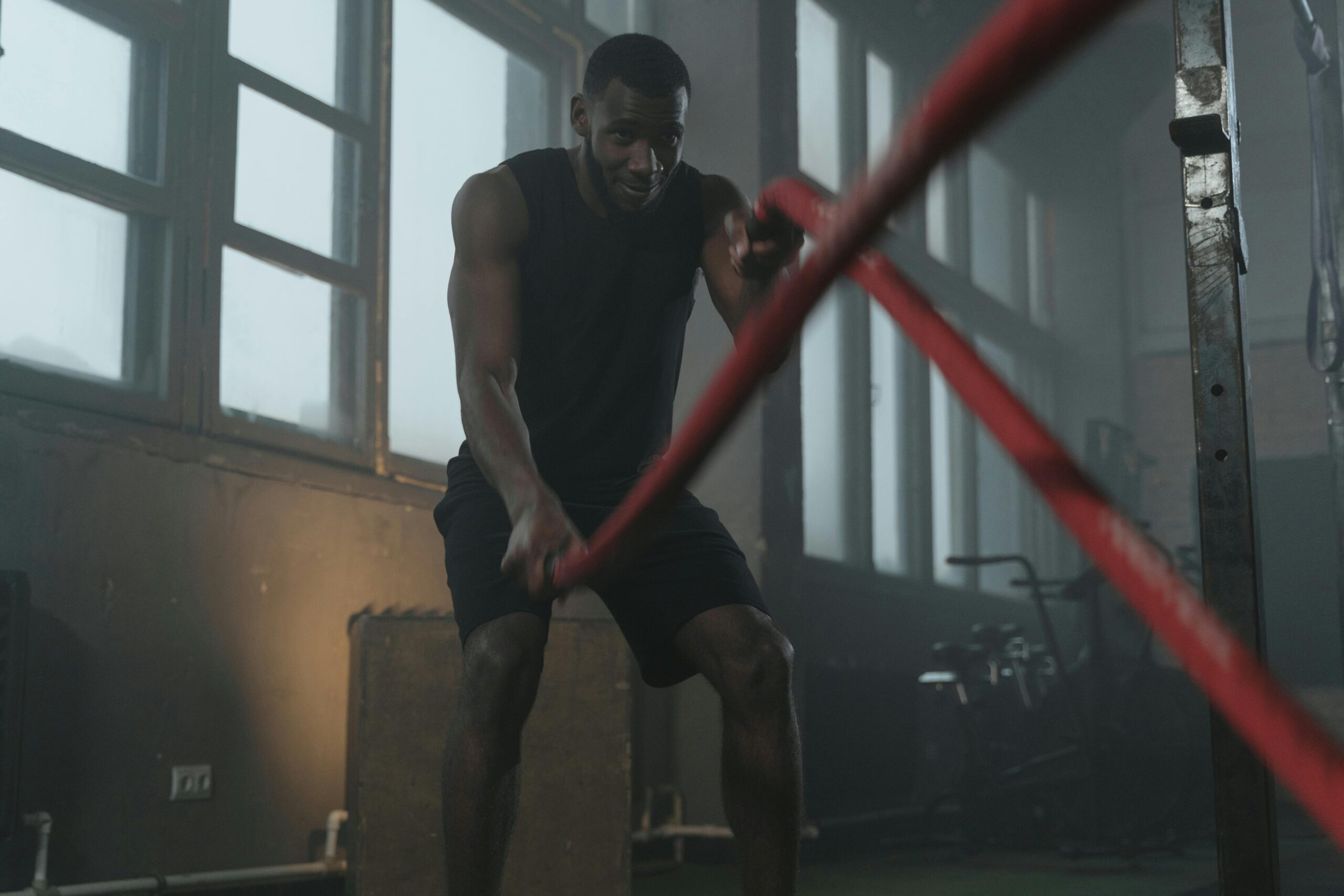 In the gym, a man pulls on a rope, focusing on his metabolic fitness during a workout.