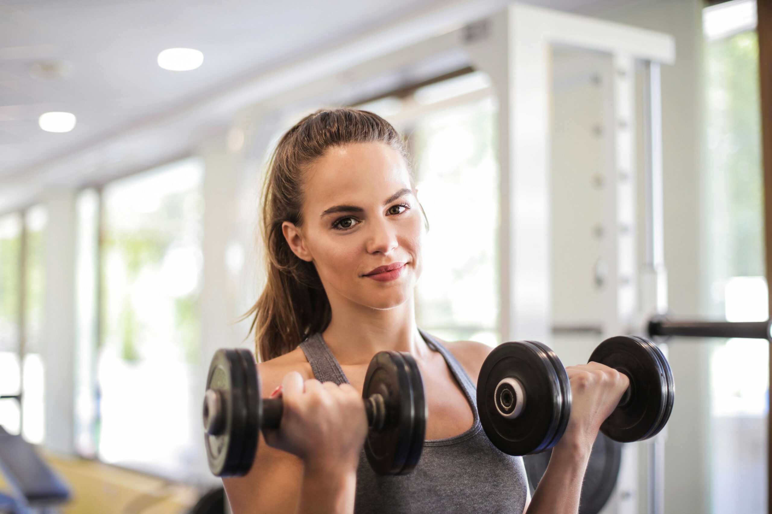 In a gym, a woman exercises with two dumbbells, emphasizing her dedication to fitness and health.